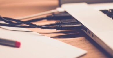 Close-up of laptop with cables on wooden desk, soft focus.