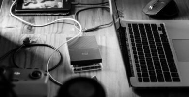 Monochrome home office scene featuring a laptop, tablet, and gadgets on a wooden desk.