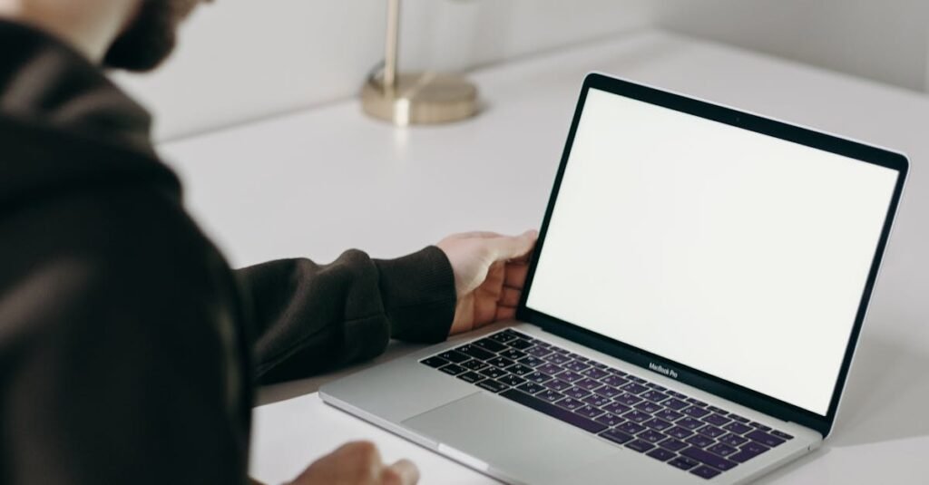 Adult man in hoodie using laptop at home with blank screen. Minimalist home office setting.
