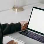 Adult man in hoodie using laptop at home with blank screen. Minimalist home office setting.