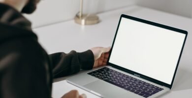 Adult man in hoodie using laptop at home with blank screen. Minimalist home office setting.