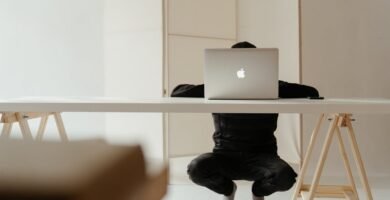 A person working in a minimalistic home office setup with a laptop on a white table.
