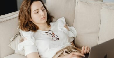 Woman lying on a couch working remotely on a laptop, embodying a comfortable home office setting.